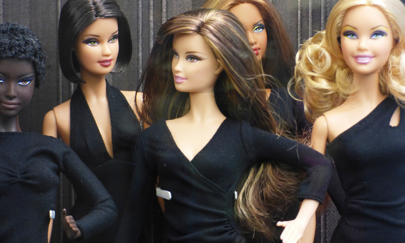 This image shows a variety of Latin Barbie dolls, with different styles, wearing black clothes.