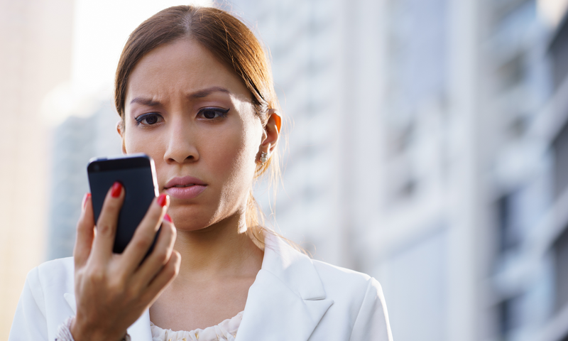 Latina woman in a white blazer gripping a mobile phone.