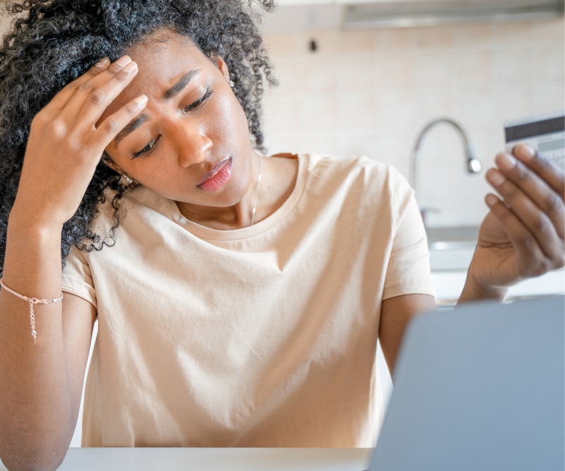 Worried Afro-Latina clutches credit card, hand on head, facing financial woes