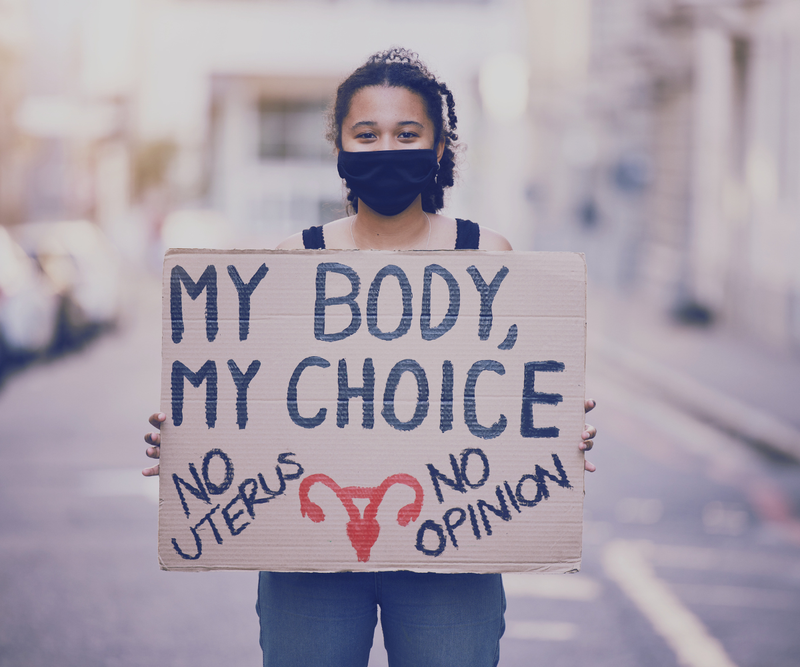 Protestor holding 'My Body, My Choice' sign with 'No Uterus, No Opinion' message, advocating for reproductive rights.